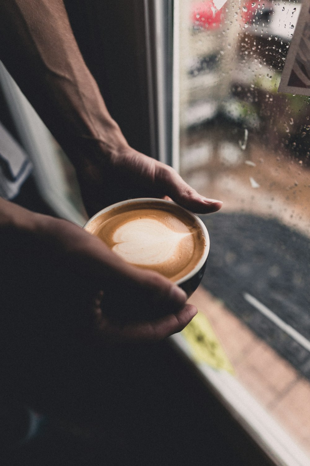 ガラス窓のそばでコーヒーの入ったカップを持っている人