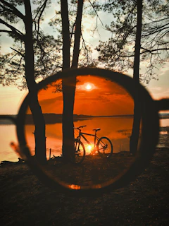 A sunset scene with a child silhouetted on a bike, the sky painted in warm reds and oranges.
