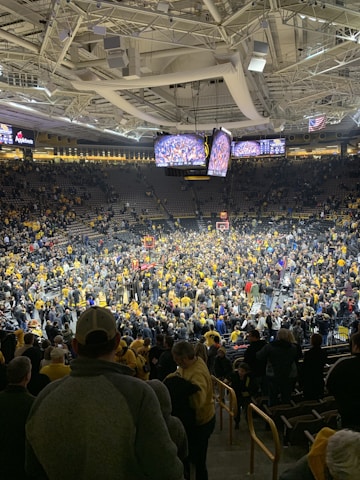 A lively crowd cheering in a basketball arena under bright lights.