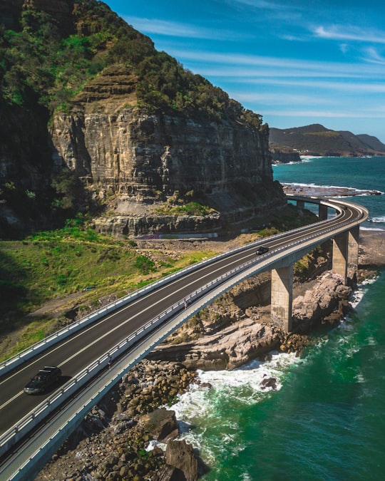 bridge road above shore near mountains during day in Sea Cliff Bridge Australia