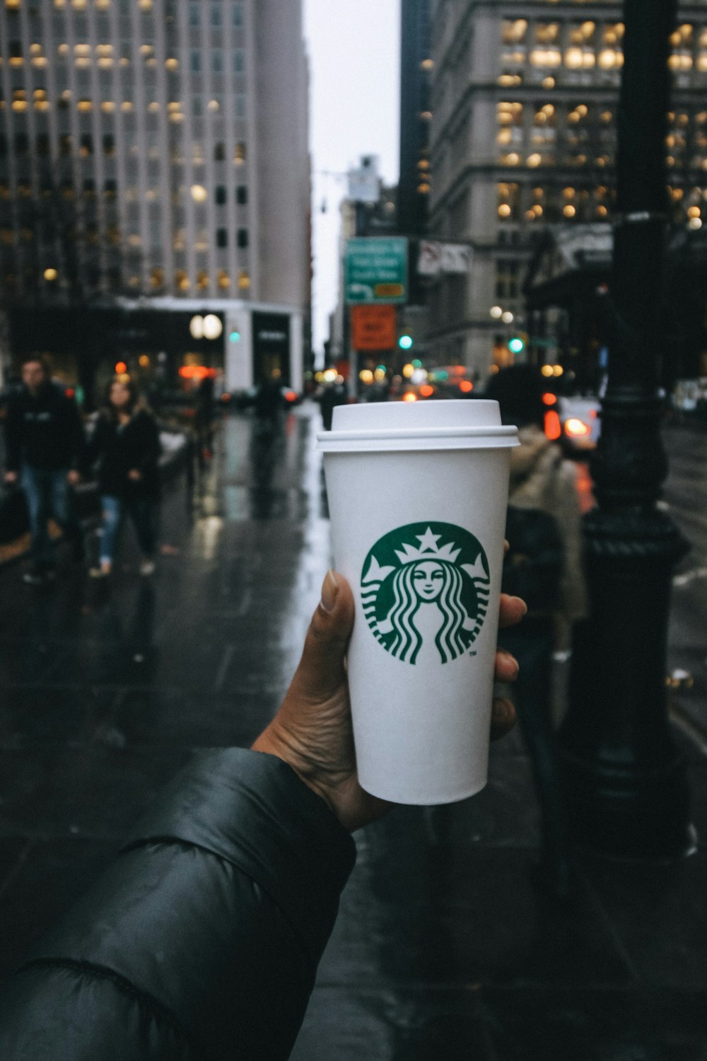 person holding Starbucks tumbler in the street selective focus photography