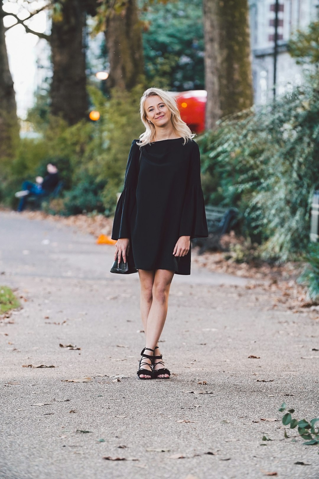 woman wearing black dress walking in the street near green shruns