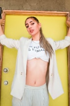 A person wearing a light-colored blazer and striped pants holds onto a door frame with a confident posture. Their shirt reads 'The Future is Female' and the backdrop is a vibrant yellow door.