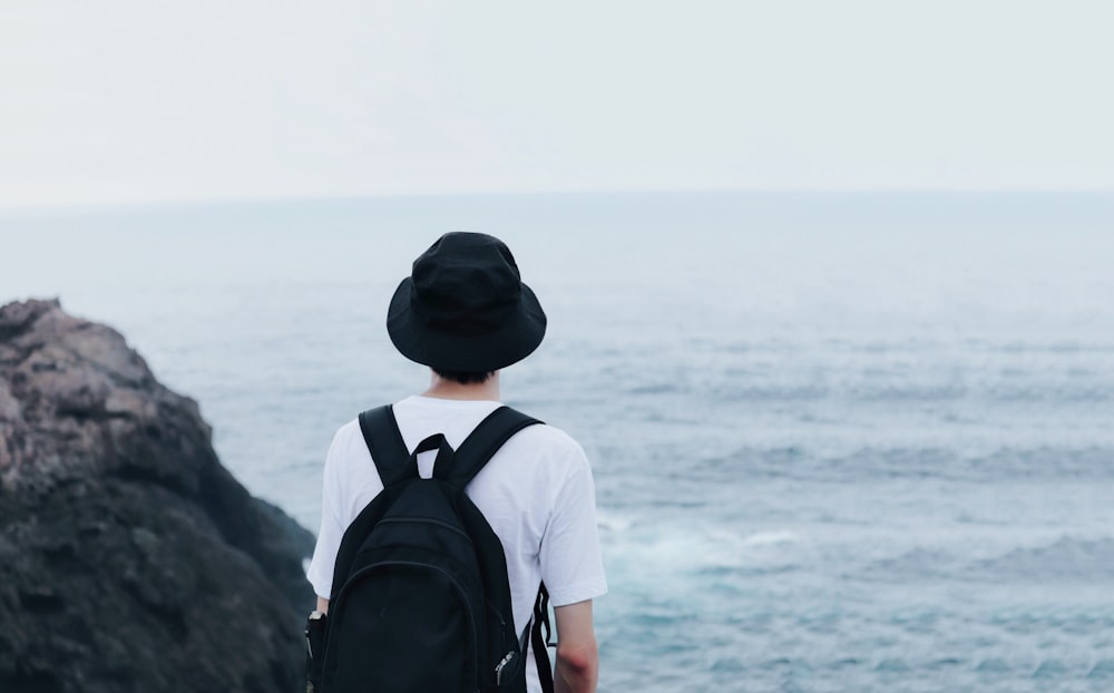 man wearing backpack and bucket hat looking the sea