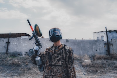 man wearing mask holding paintball gun during daytime