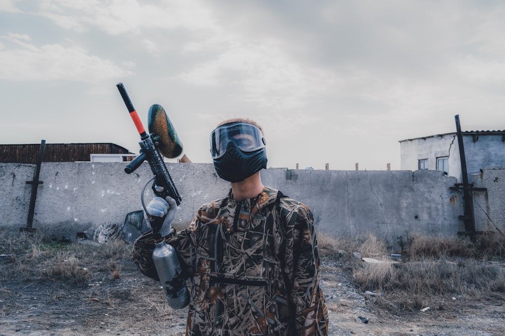 man wearing mask holding paintball gun during daytime