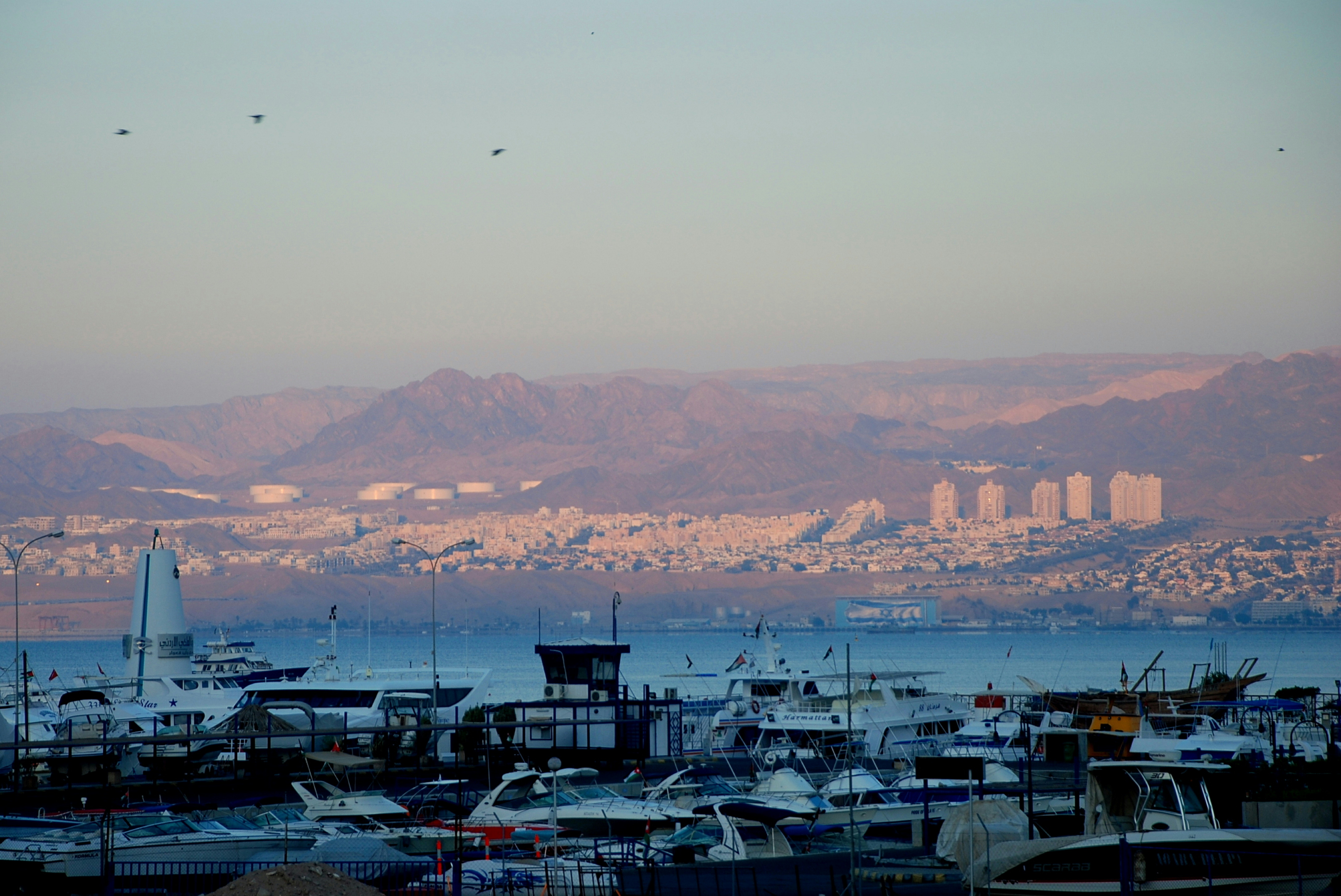 A panoramic shot of the Aqaba shoreline In Jordan. The Red Sea appears as a vibrant blue colour with the red, rolling mountains in the background.