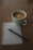A white cup of coffee sits on a wooden table next to a spiral-bound notebook with a pencil resting on top. The notebook page contains a checklist with one item marked as complete and another yet to be checked.