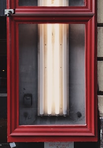 A rectangular red frame encloses a set of vertical fluorescent lights mounted against a wall. There is a small device installed on the left side within the frame. The lower section of the image includes partial text on a sign about an automatic sprinkler shut-off valve.