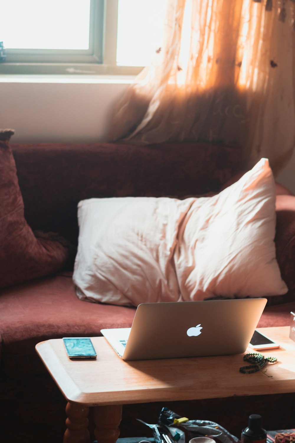 赤いソファに白い枕、木製のコーヒーテーブルの上にiPhoneの近くにMacBook Airを
