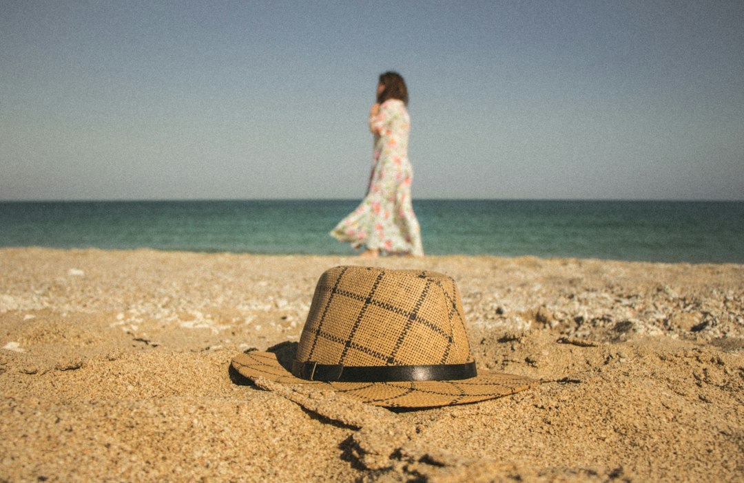 woman walking near seashore and brown and gray hat on brown sand,