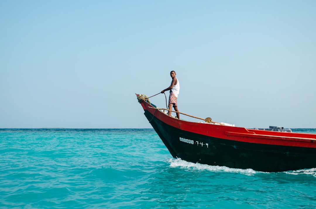 man wearing white tank top riding black and red canoeboat