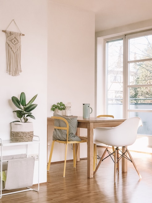 A maximalist dining area featuring a muted yellow vintage rug, colorful patterned chairs, and an array of potted plants on a rustic wooden table.