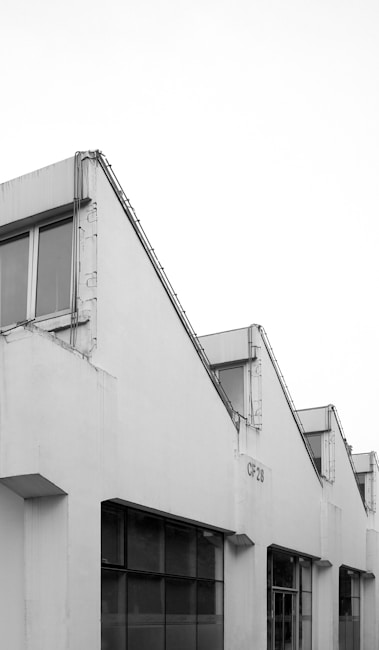 A minimalist architectural structure with a series of connected gabled roofs, featuring large windows and stark white surfaces. The design is industrial and functional.