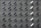 A grid pattern of surveillance cameras is mounted on a gray brick wall. Most of the cameras are black, with a few white ones interspersed, all angled uniformly to the left.
