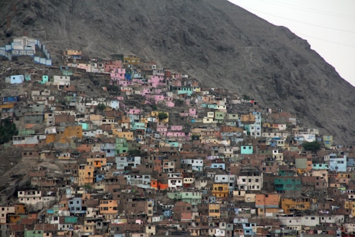 Colorful houses densely packed on the side of a steep, rocky hill, creating a vibrant yet crowded urban landscape. The structures are a mix of bright colors such as pink, blue, yellow, and green, standing out against the muted tones of the brown rocky terrain.