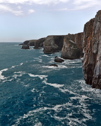 A dramatic coastline with rugged cliffs meeting deep navy blue ocean waves.