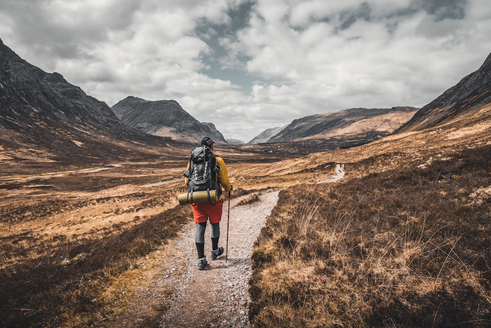 person wearing backpack walking on dirt road