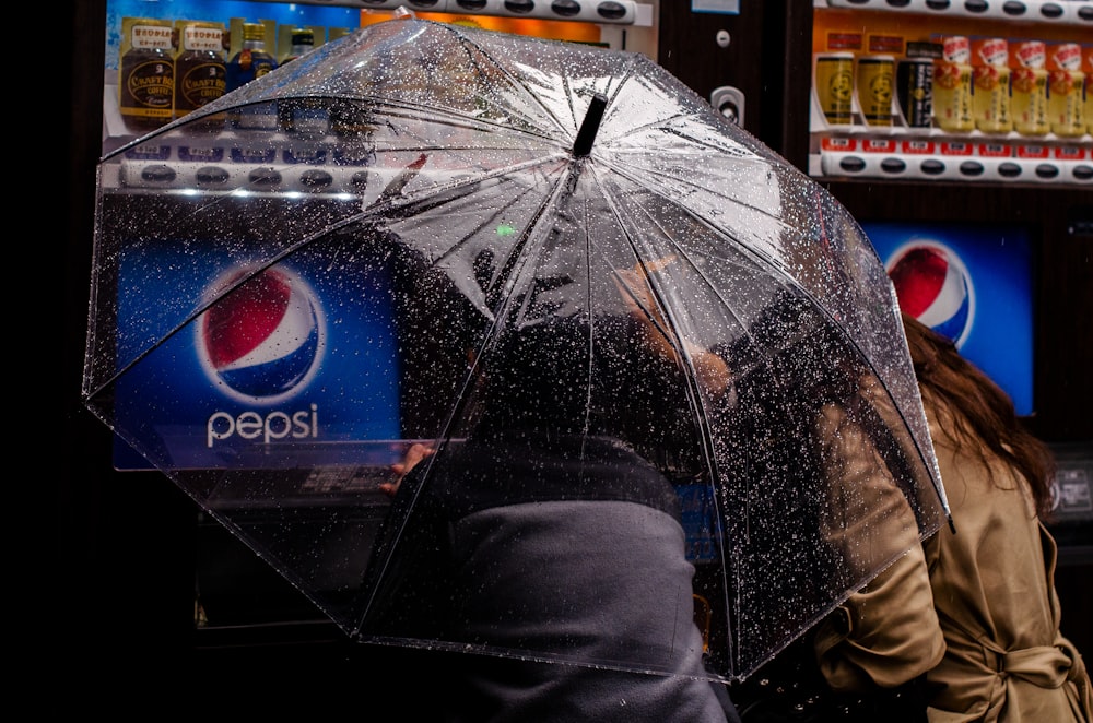 personne sous un parapluie en plastique transparent près d’un distributeur automatique Pepsi