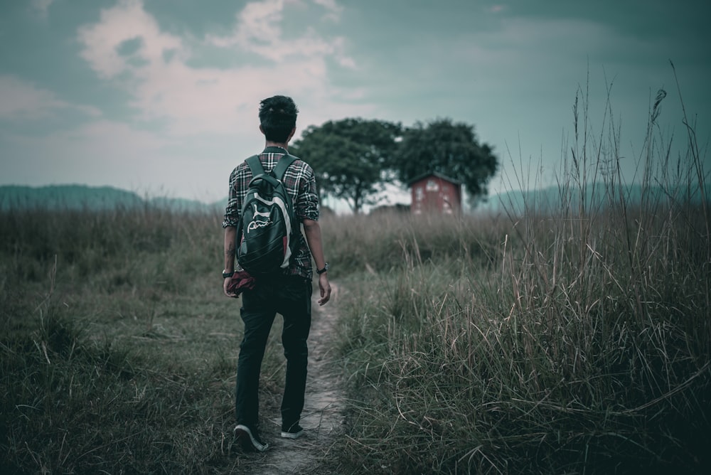 man walking on road in between grass field during daytime