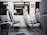 A row of empty seats inside a train or subway car, with blue and white upholstery. The interior is clean and modern, featuring metal armrests and windows reflecting the outside scene. A sign in the corner suggests reserved seating.