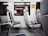 A row of empty seats inside a train or subway car, with blue and white upholstery. The interior is clean and modern, featuring metal armrests and windows reflecting the outside scene. A sign in the corner suggests reserved seating.