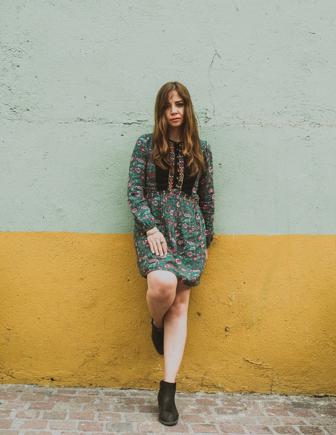 woman in green floral dress standing and leaning on concrete gray painted wall during daytime