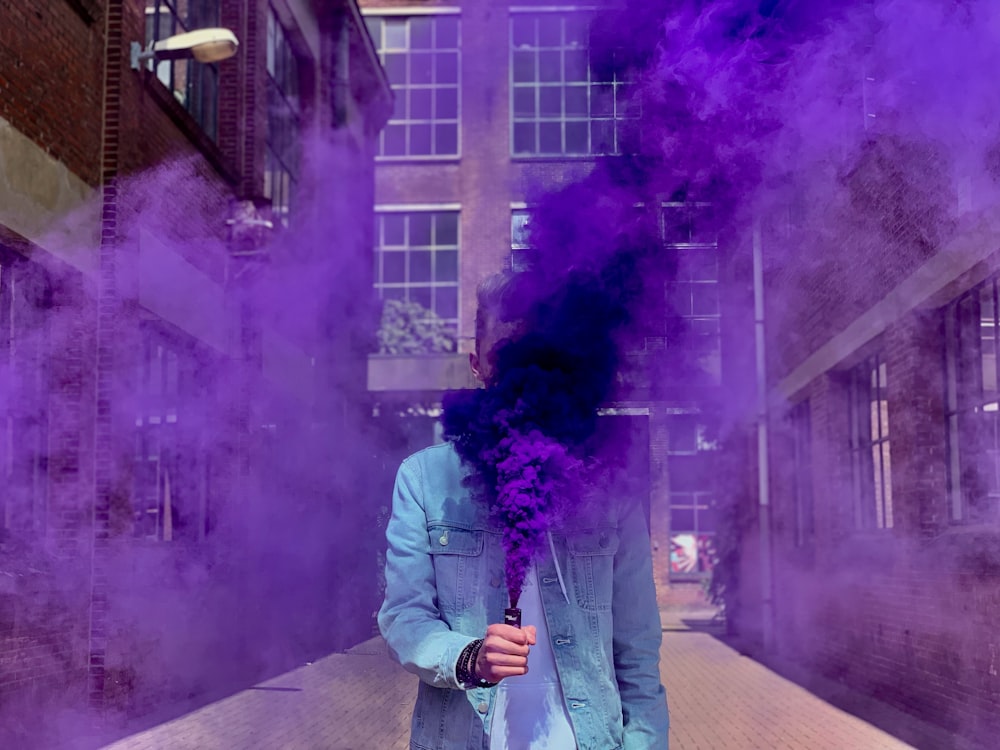 person in blue denim jacket putting smoke bomb near face