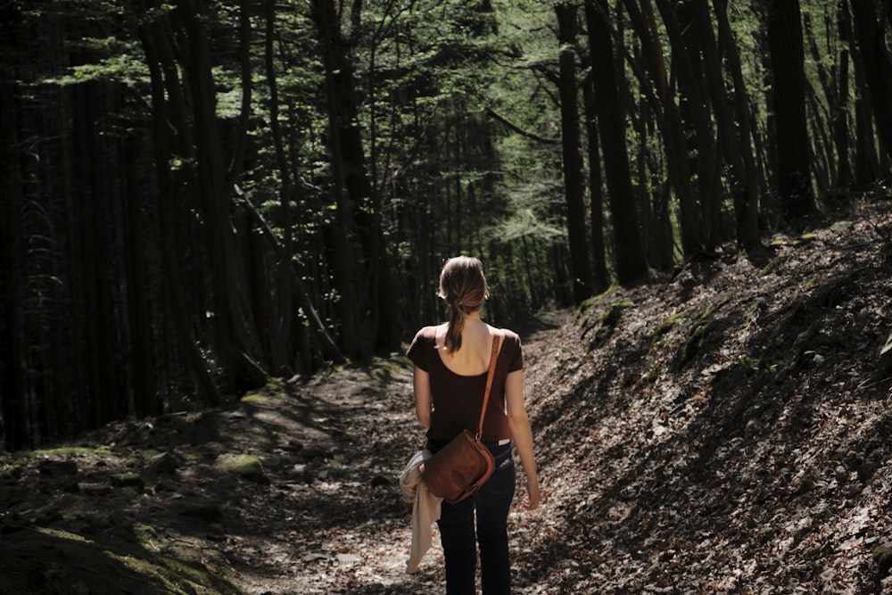 woman walking and facing back surrounded with tall and green trees