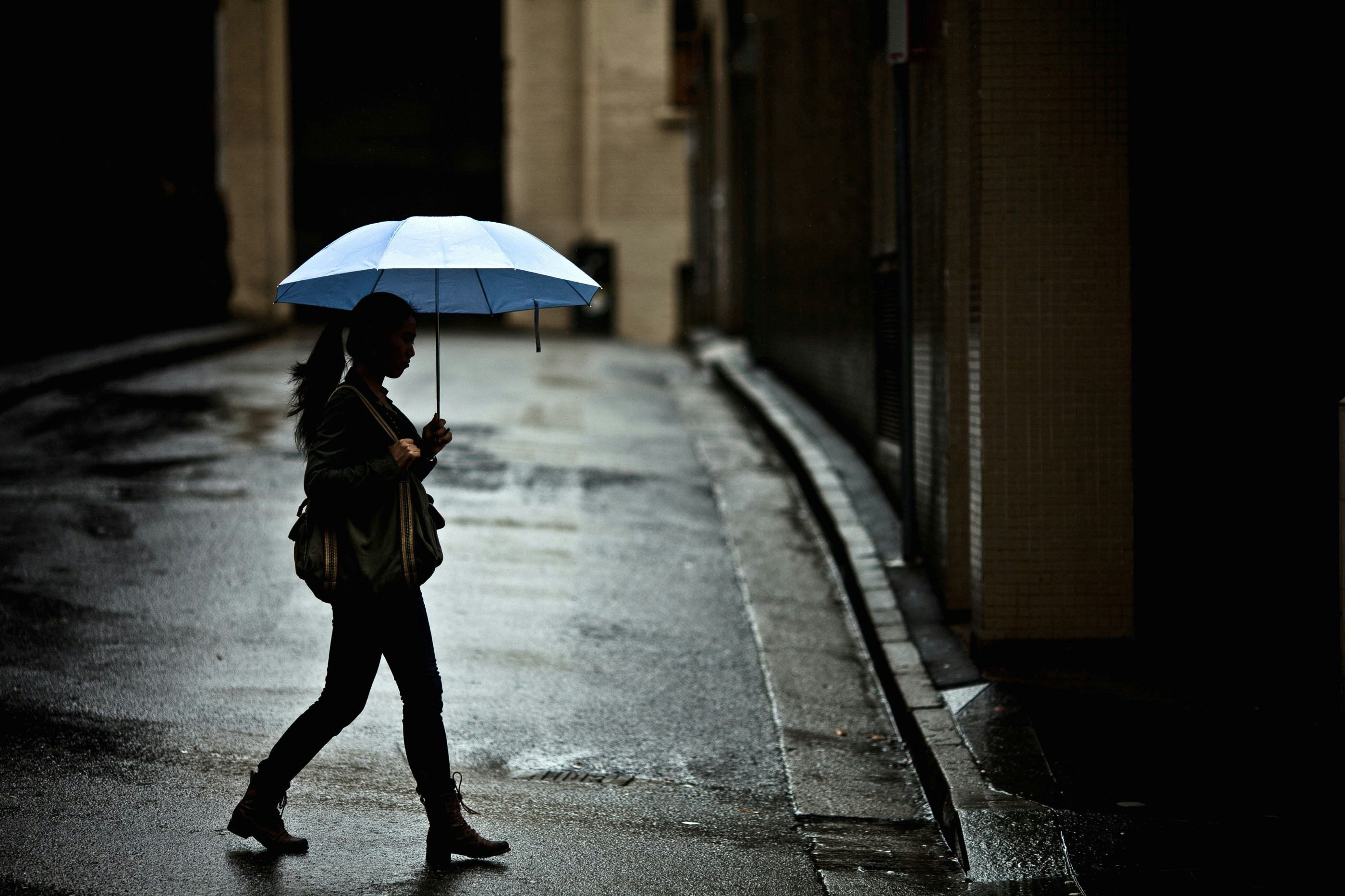 woman with tote bag holding umbrella while crossing street