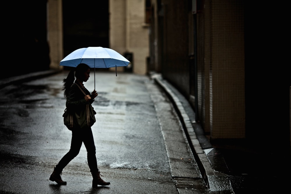 woman with tote bag holding umbrella while crossing street