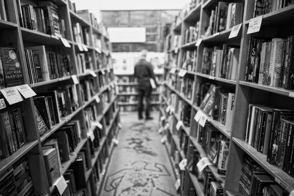 grayscale photo of man standing in front of books