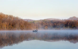 A serene early morning fishing scene by a misty lake with a lone fisherman casting a line.