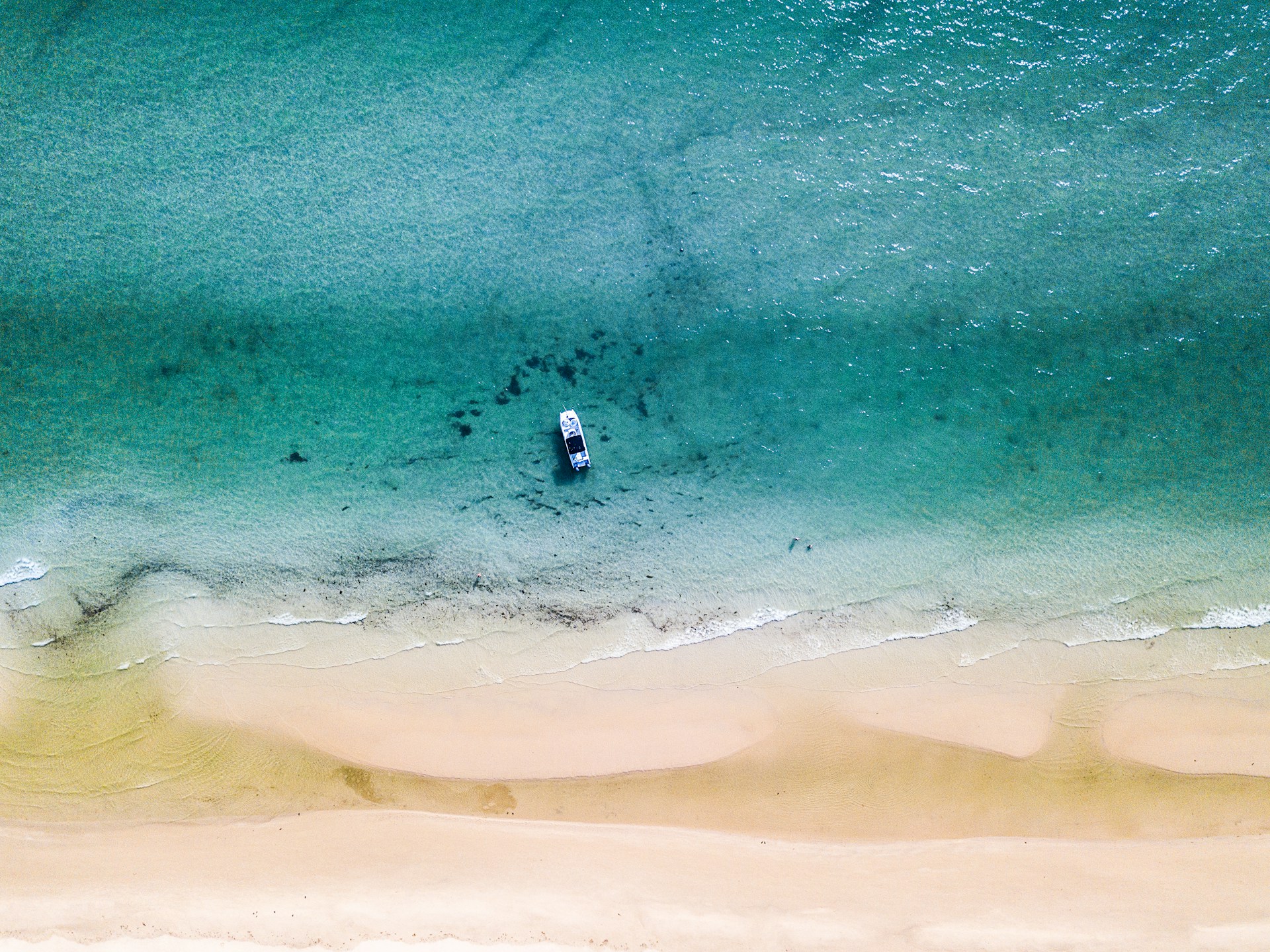 A panoramic view of a luxury boat anchored near a serene beach with turquoise water.