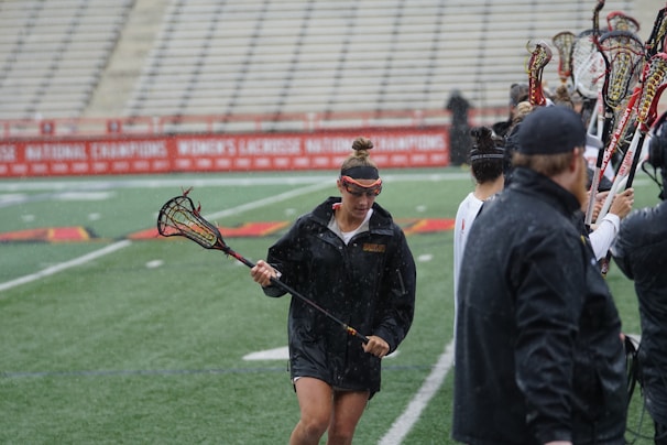 A hockey team celebrating a goal with sticks raised high on a rain-soaked field.