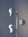 A vertical metal structure with two white, modern lamp fixtures attached with circular heads. The lighting design is minimalistic, with a soft, ambient light surrounding the fixtures that creates a subtle and calm atmosphere.
