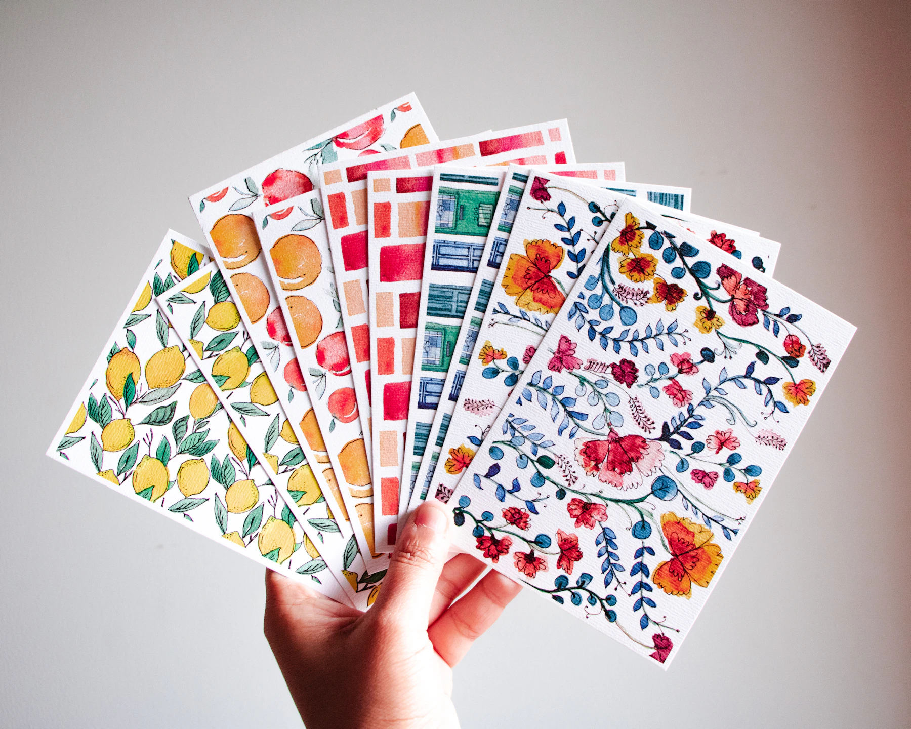 A hand holding a fan of cards printed with floral and fruit patterns