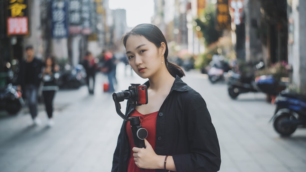 woman holding gimbal with camera standing in the middle of the road near people and motorcycles