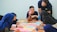 A group of people sitting around a table engaged in a discussion, with colorful sticky notes spread out in front of them. One person is pointing at a note, while others listen attentively. The setting appears to be a collaborative environment, possibly a workshop or brainstorming session.