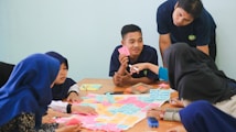 A group of people sitting around a table engaged in a discussion, with colorful sticky notes spread out in front of them. One person is pointing at a note, while others listen attentively. The setting appears to be a collaborative environment, possibly a workshop or brainstorming session.