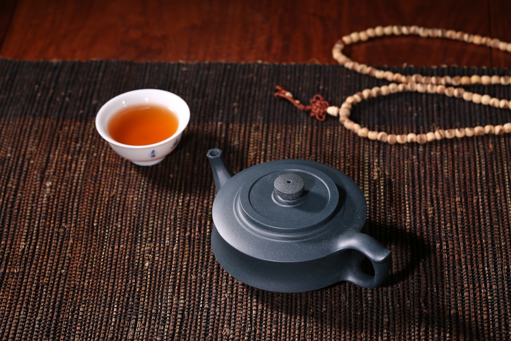 white ceramic teacup beside black ceramic teapot