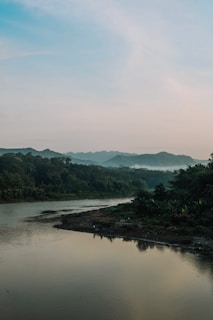 A serene landscape showing a clean river flowing through a forest at sunset.
