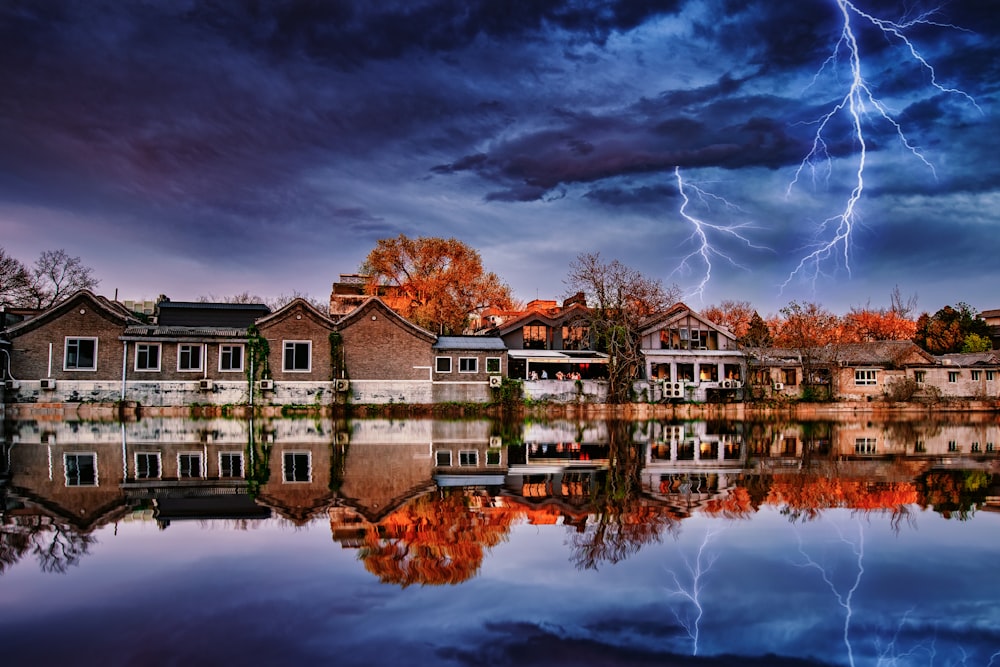 reflection of houses on body of water under dramatic clouds