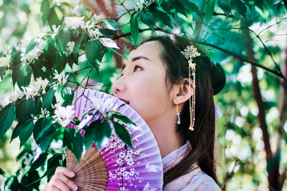 Mujer sosteniendo un abanico debajo del árbol