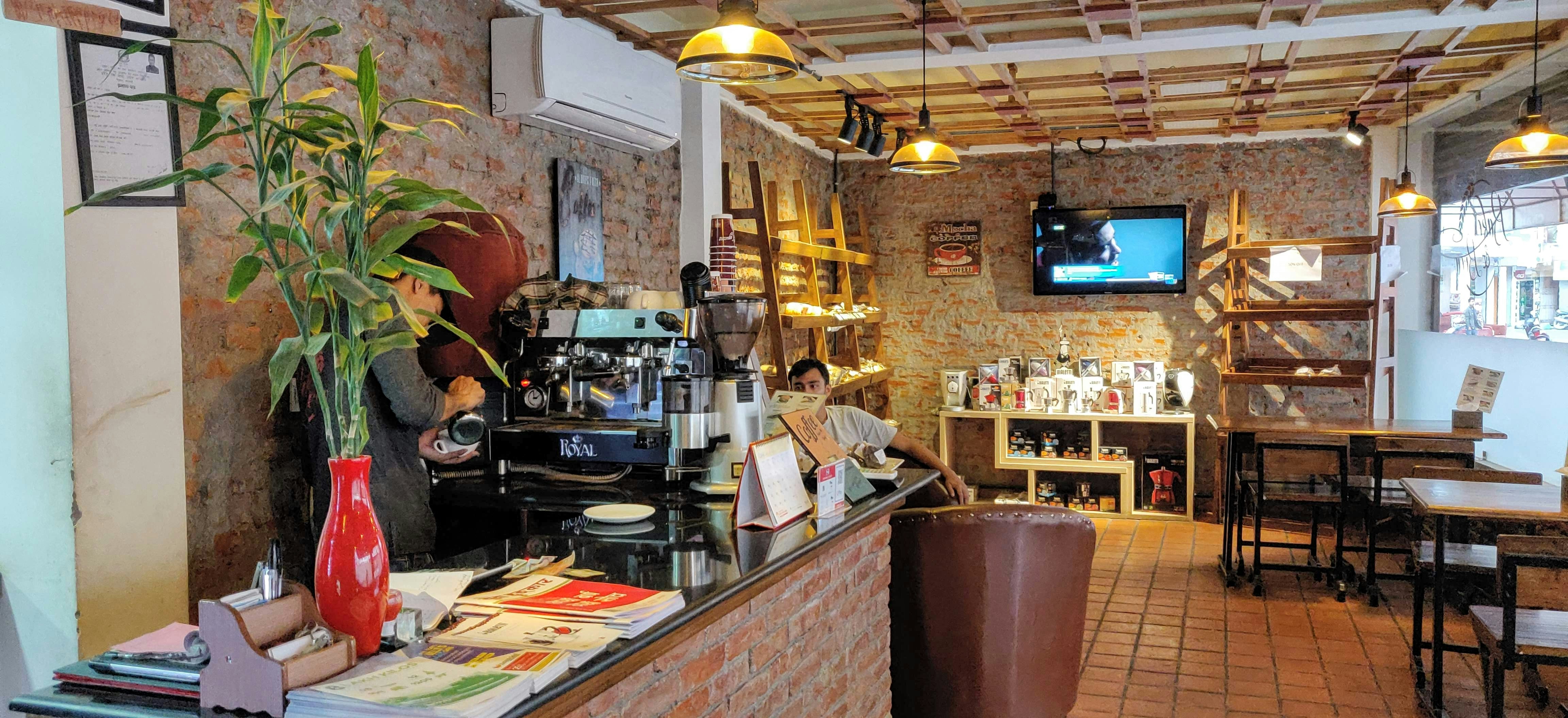 Cozy café interior with warm amber lighting, people working on laptops, ceramic coffee cups, exposed brick walls, slow morning atmosphere
