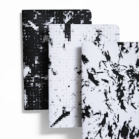 A set of three notebooks with abstract, pixelated black and white covers arranged in a staggered layout. The covers feature a mixture of geometric and organic patterns, creating a modern visual effect.