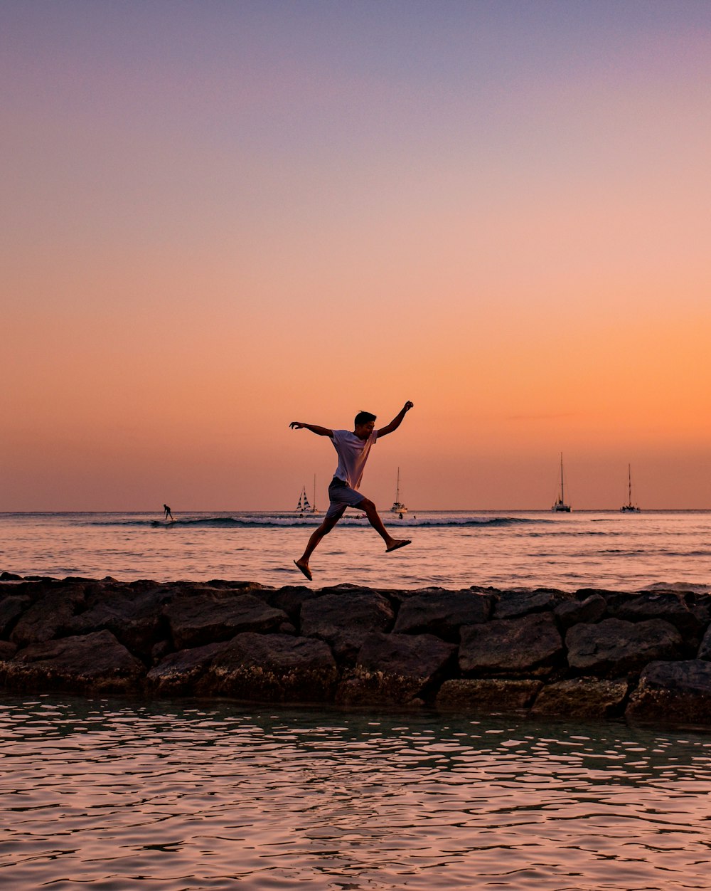 men's white shirt walking on rock beside body of water during golden hour