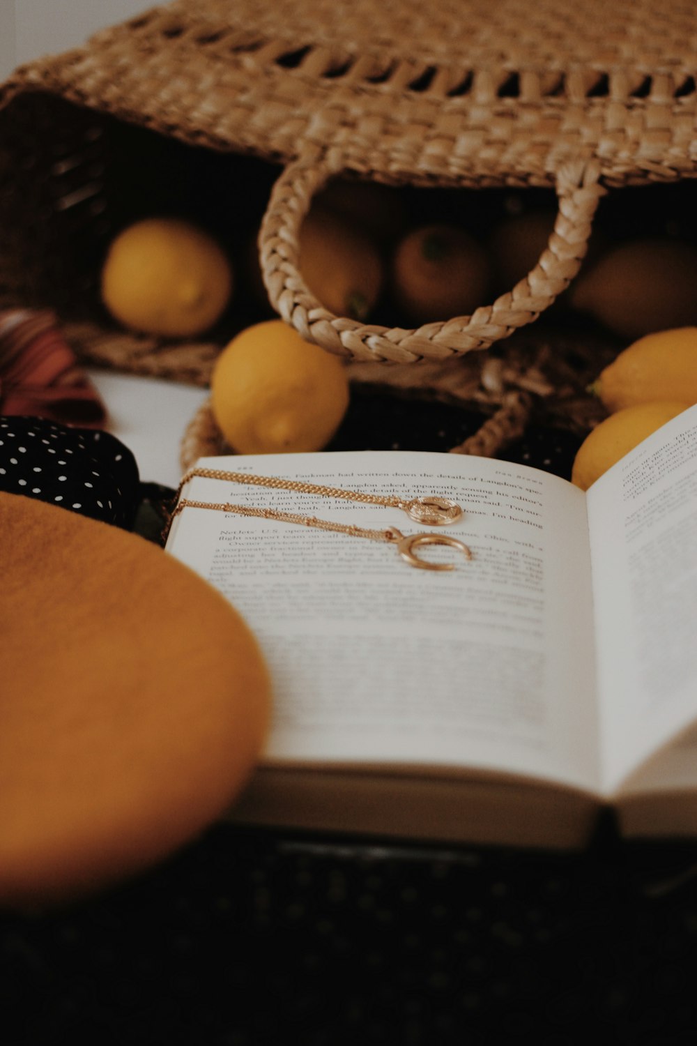 two gold-colored necklaces on opened book beside lemon in basket