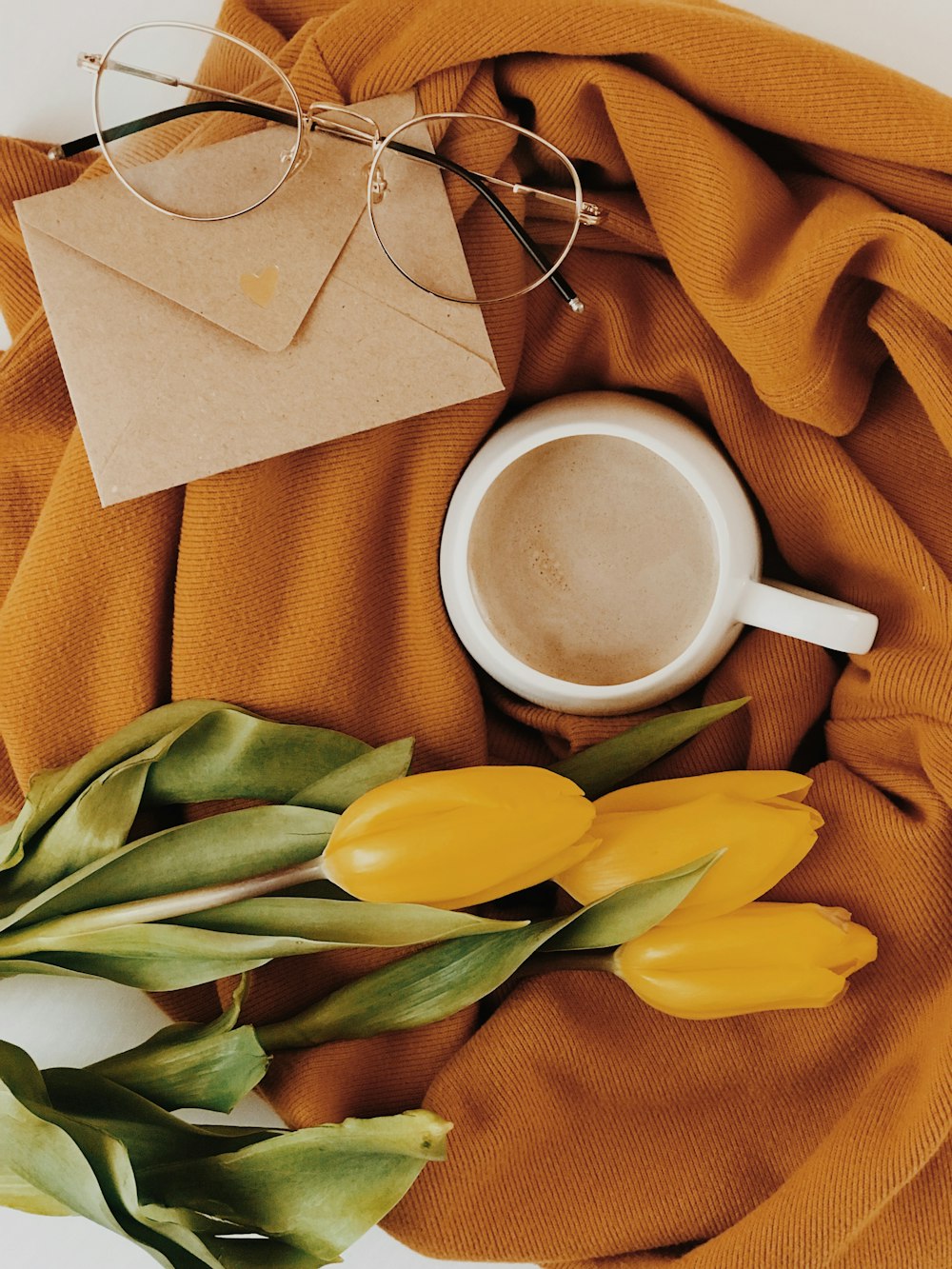 tazza, occhiali, fiori e busta su tessuto marrone