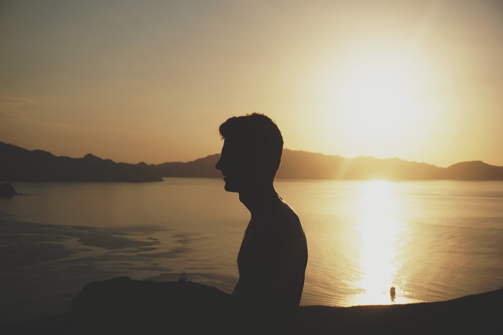 Silhouette eines Mannes neben einem Gewässer während der goldenen Stunde